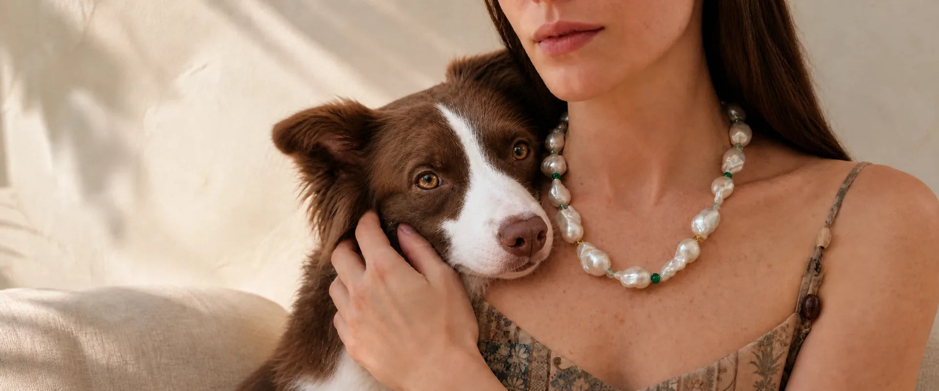 Woman wearing a baroque pearl necklace while holding her brown and white border collie