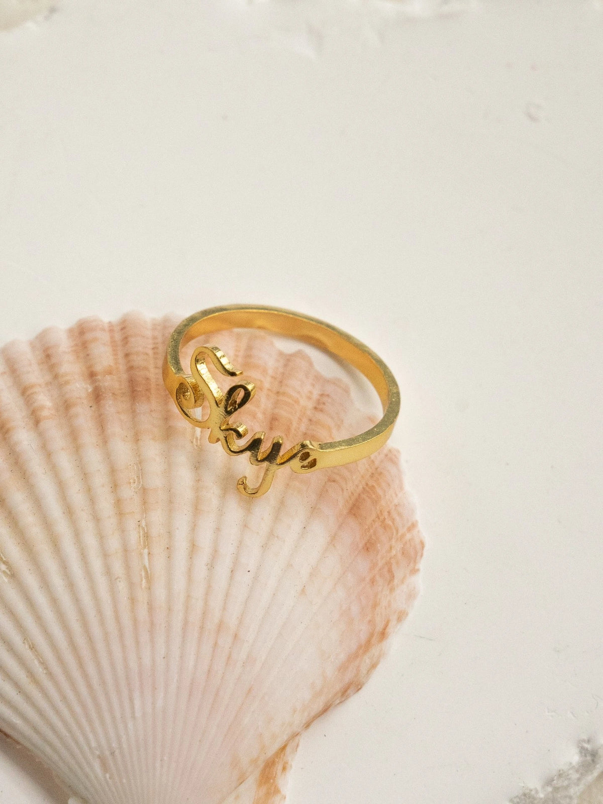 Gold personalized Skye name ring resting on a seashell
