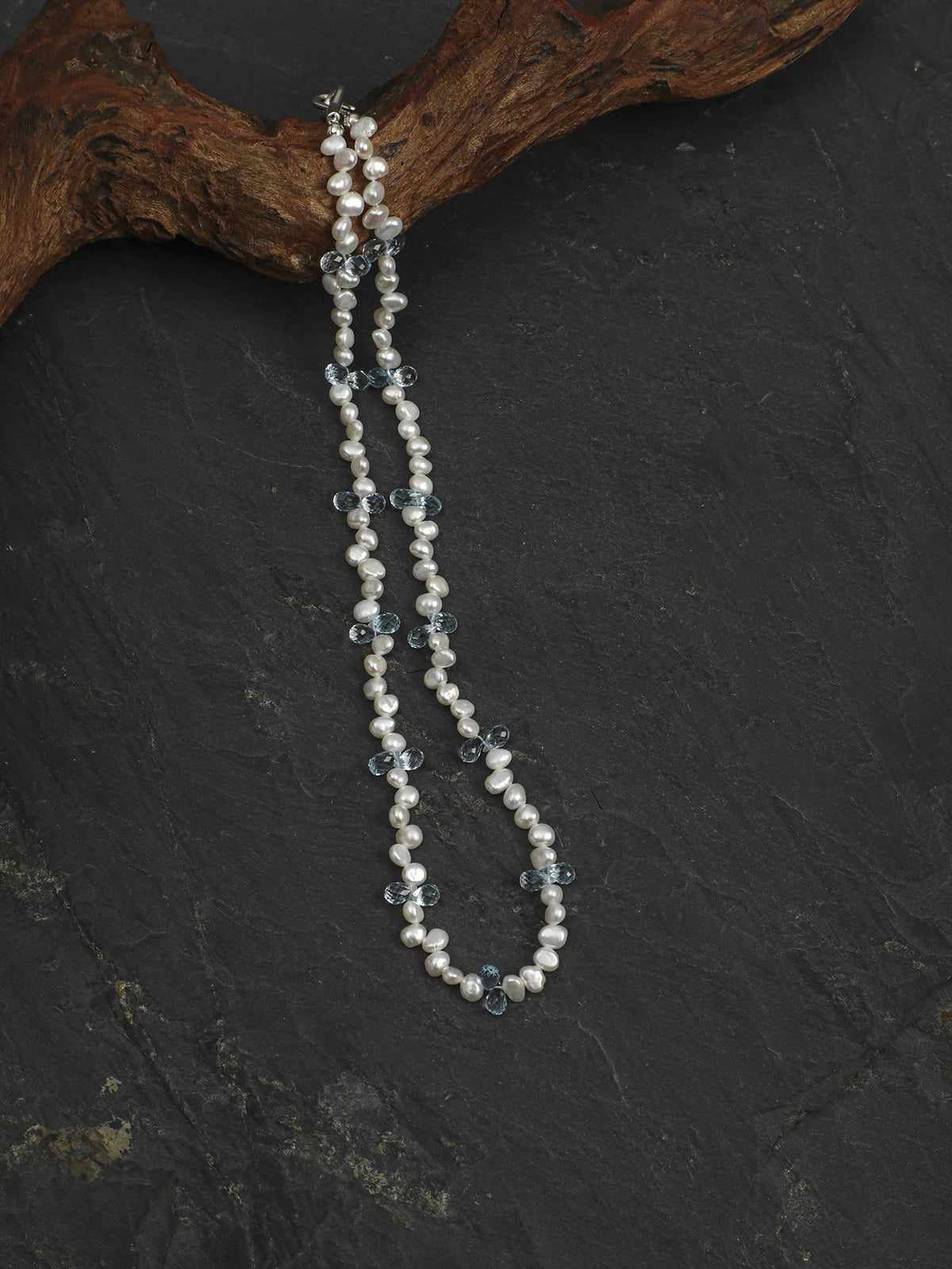 Pearl and blue topaz necklace suspended from a wood display