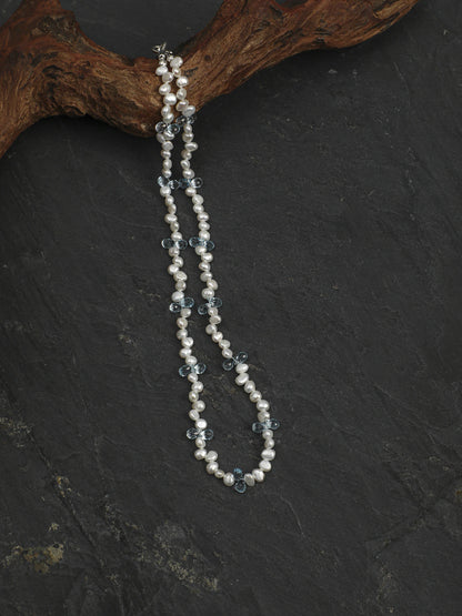 Pearl and blue topaz necklace suspended from a wood display