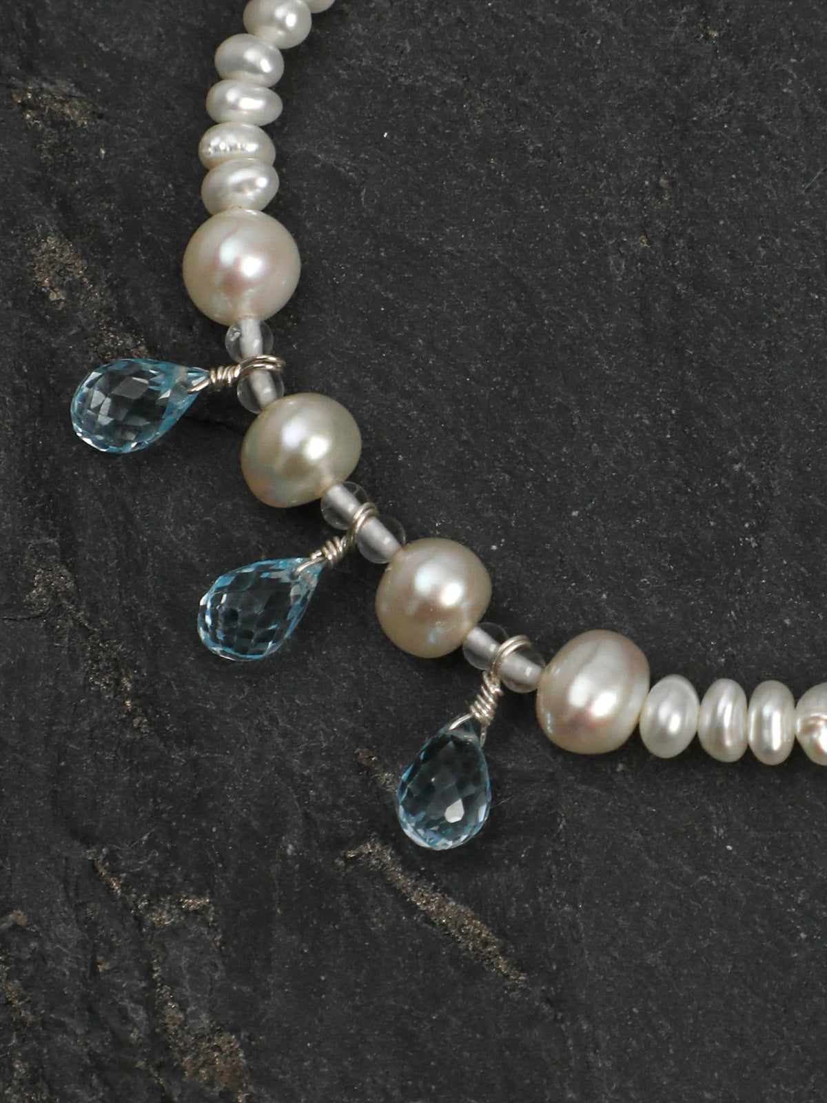 Close-up of three dangling teardrop-cut blue topaz gems and pearls on the Ocean Tears bracelet