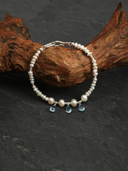 Ocean Tears pearl and blue topaz bracelet draped over driftwood and dark stone