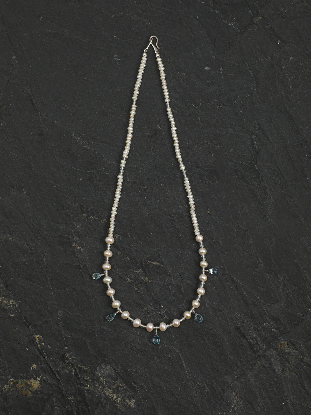 Ocean Tears pearl necklace with dangling blue topaz drops on a light background