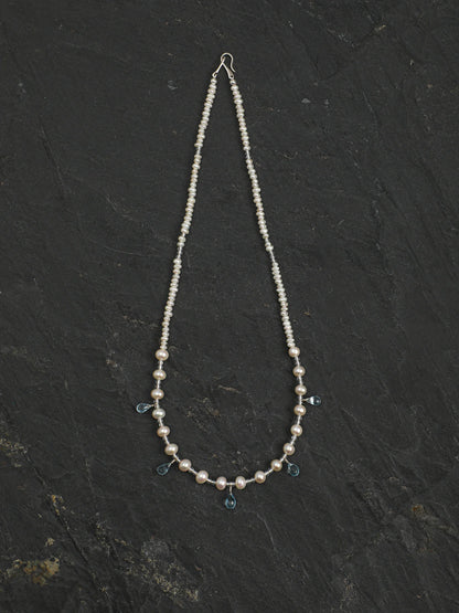 Ocean Tears pearl necklace with dangling blue topaz drops on a light background