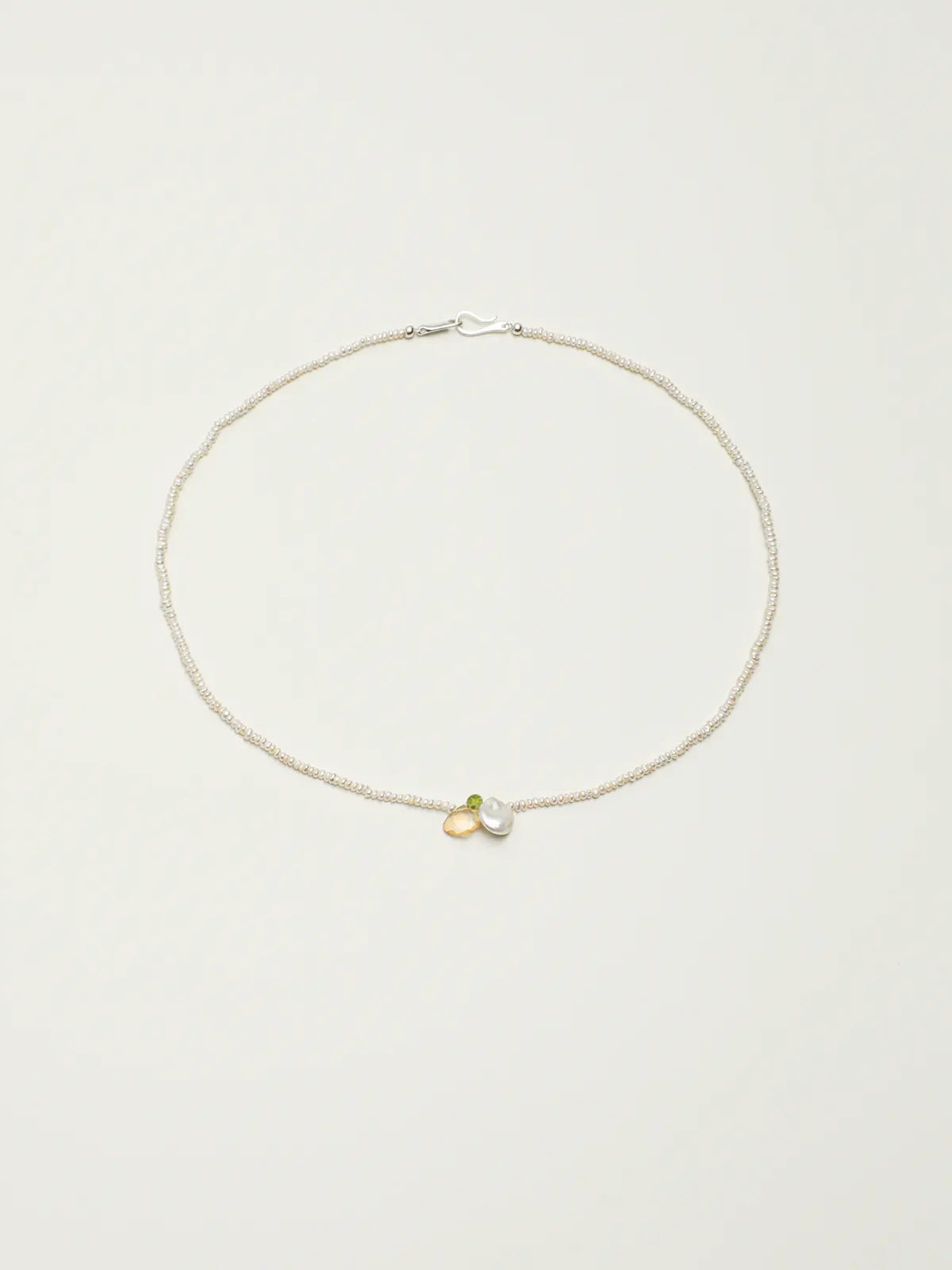 Pearl necklace with green and yellow gemstone accents on a light background
