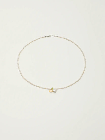 Pearl necklace with green and yellow gemstone accents on a light background