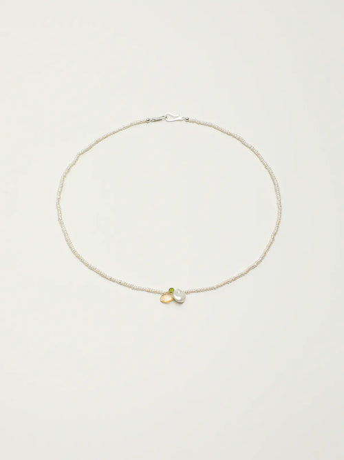 Pearl necklace with green and yellow gemstone accents on a light background