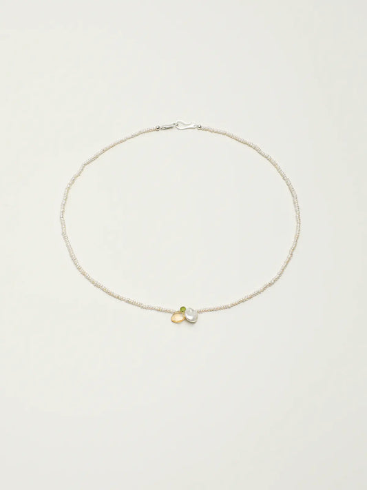 Pearl necklace with green and yellow gemstone accents on a light background