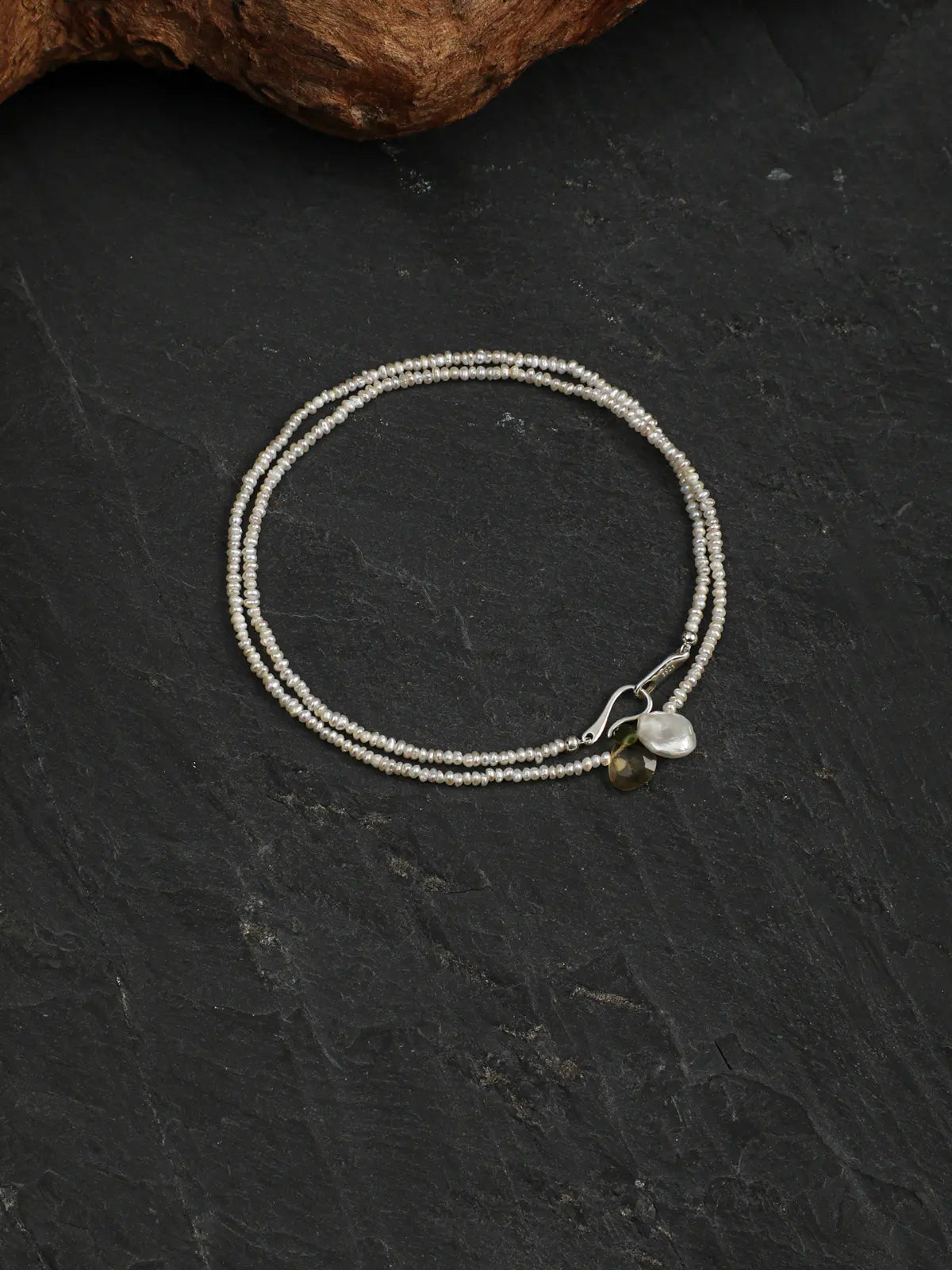 Pearl necklace arranged in a loop on dark stone