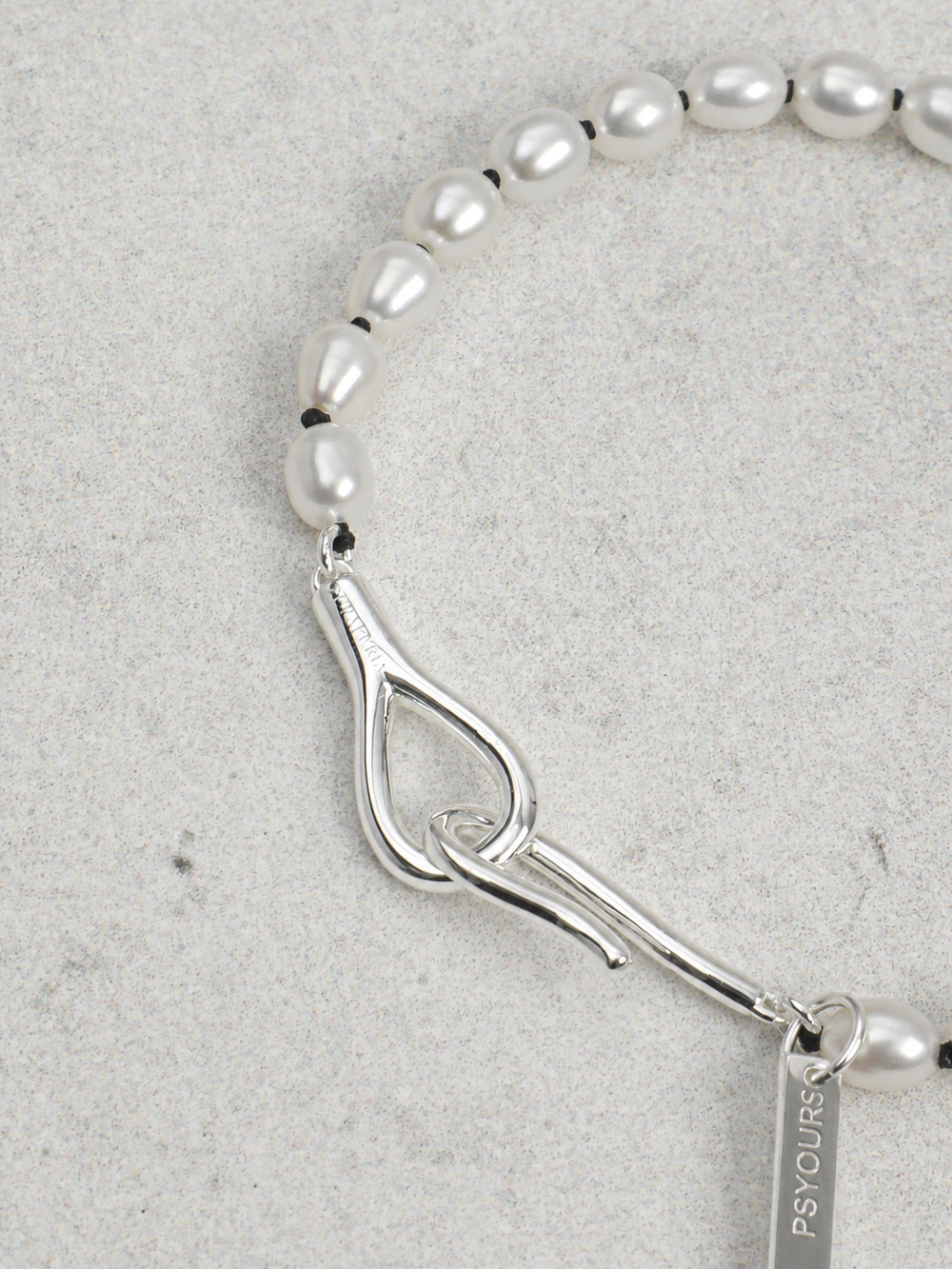 Engraved silver tag and clasp detail on a Psyours pearl piece, shown as a craftsmanship example.