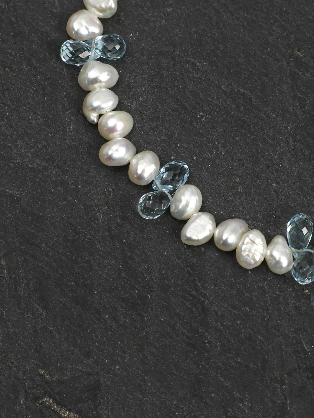 Close-up of baroque pearls and faceted blue topaz beads on a dark stone surface