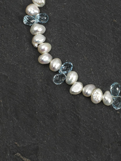 Close-up of baroque pearls and faceted blue topaz beads on a dark stone surface